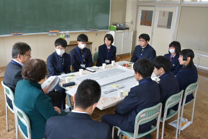 模造紙が置かれたテーブルを囲むように議員の方と参加学生が座り、男性議員の話を真剣に聞いている写真