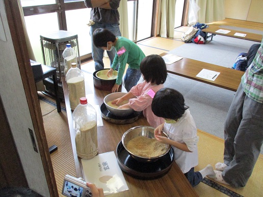 長机に米が入ったボウルが3つ並べられ、それぞれに子どもたちが手を入れて観察している写真