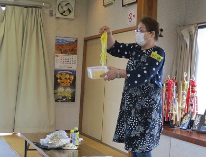 女性が手に持った容器からそうめんかぼちゃをつまみ上げて見せている写真