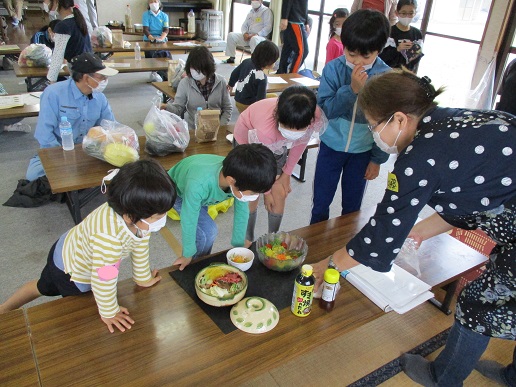 長机の上に置かれた3種類の料理を興味津々でのぞき込む子どもたちの写真