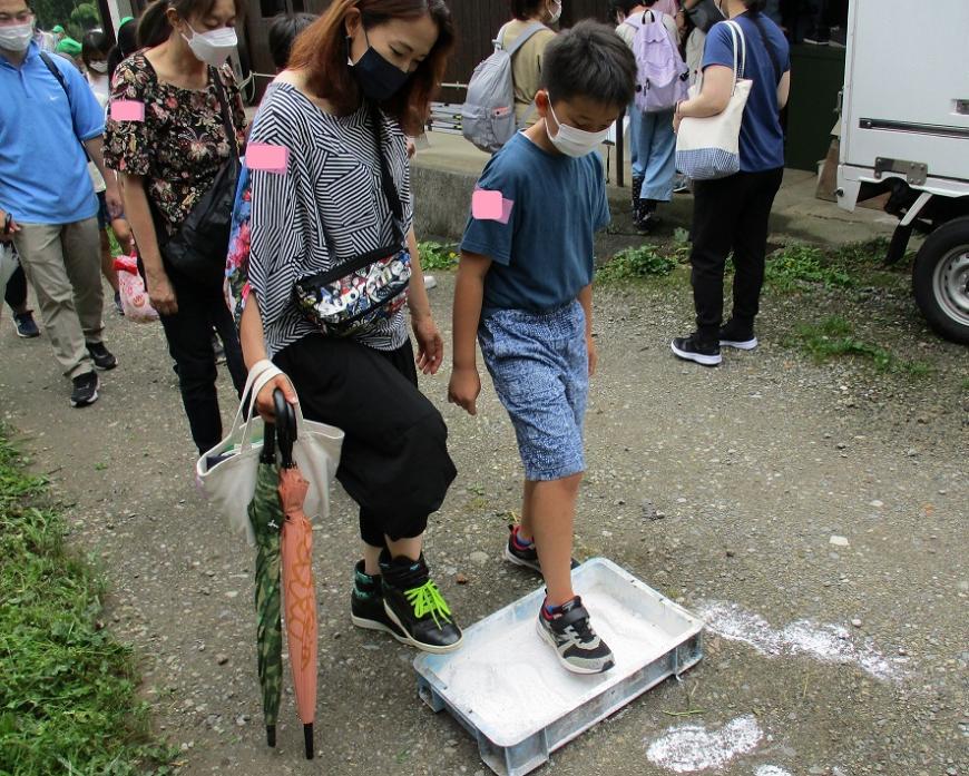 地面に置かれた四角い容器に入った石灰に、片足ずつ靴底をつけている親子の写真