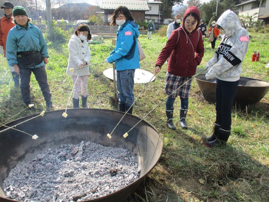 炭化器の中の炭に竹串に刺したチーズをかざす参加者たちの写真