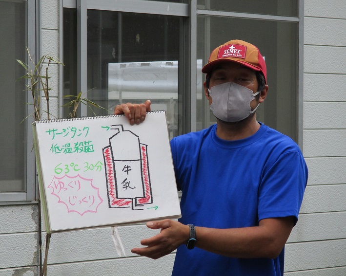 サージタンクの説明とイラストが描かれた画用紙を持った青いTシャツを着た男性の写真