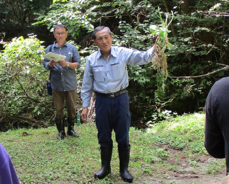 根のついたワサビを片手に持って参加者に見せている男性の写真