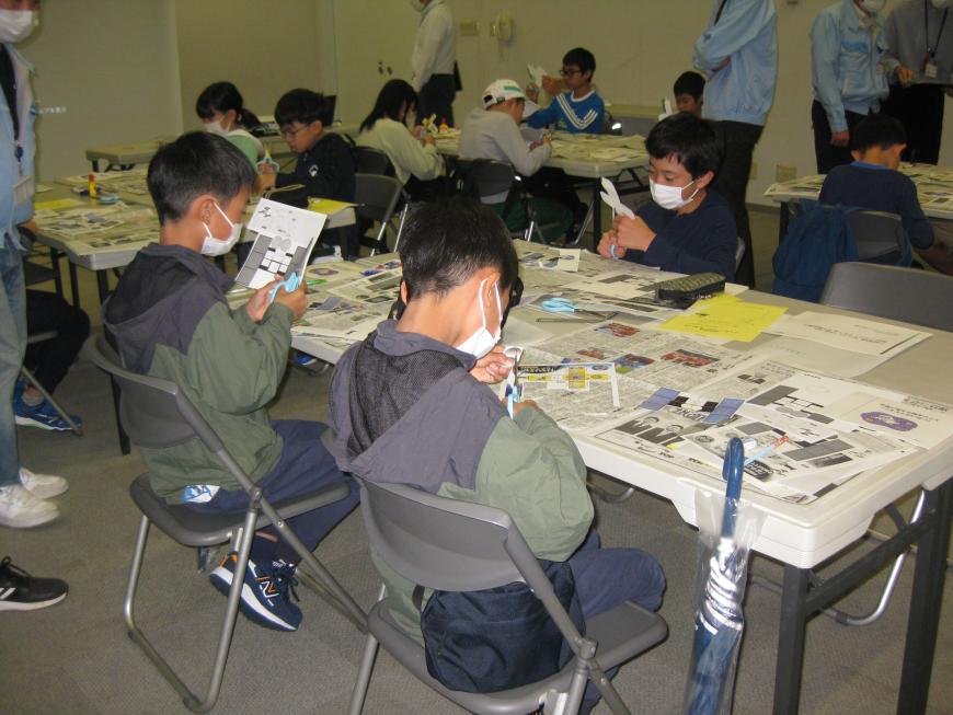 参加者の子ども達がグループごとに分かれてテーブルに座っており、テーブルの上には沢山の資料が置かれ、はさみで紙を切り抜き、ペーパークラフトの作成をしている様子の写真