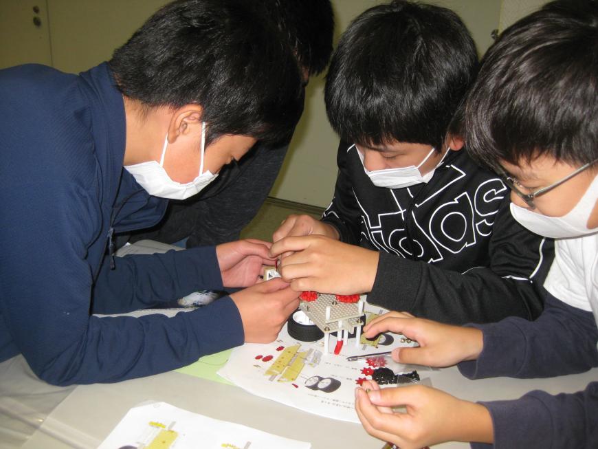 宇宙エレベーターを作る為に男の子4名が頭を突き合わせて説明書を見ながら部品の組み立て作業を行っている様子の写真