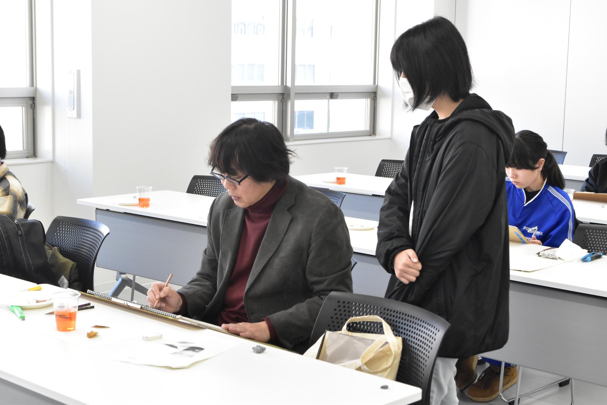 齋氏よりデッサン指導を受ける様子