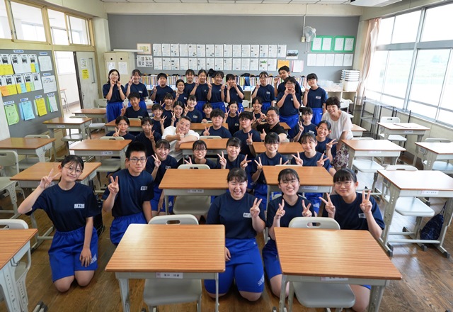 教室に菊本和昭氏、竹島悟史氏、生徒の皆さんが笑顔でピースサインをして写っている集合写真