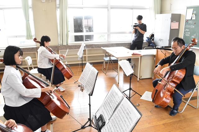 譜面台に楽譜が置かれ、チェロを持った生徒の皆さんが市寛也氏の指導を真剣な表情で聞いている様子の写真