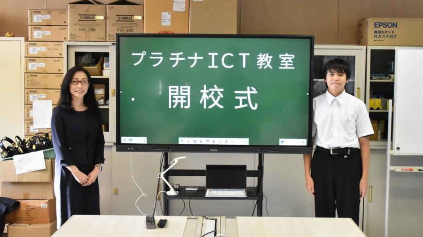 モニター画面にプラチナICT教室 開校式と表示され、両脇に株式会社エフコム二瓶常務さんと北信中学校パソコン部部長の男子生徒が立って写っている写真