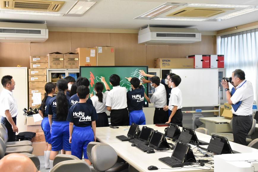 生徒の皆さんが電子黒板の前に集まり、画面に思い思いに板書している様子を写した写真