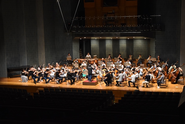 ステージ上でNHK交響楽団の皆さんが指揮者に合わせて演奏しているリハーサルの様子を写した写真