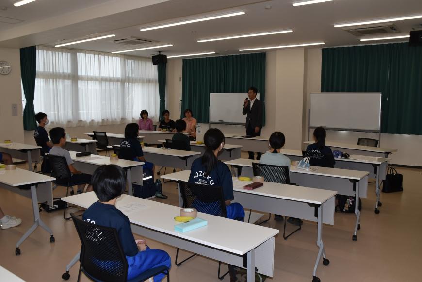 美術部員の皆さんが席についており、佐藤教育長が前に立ちマイクを持って話をしている様子の写真