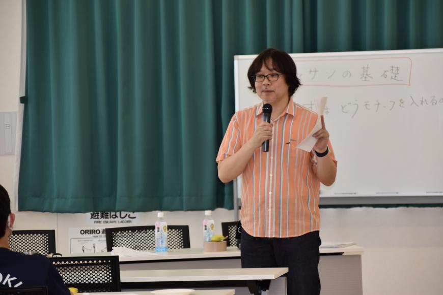齋氏がマイクを持って話をしている写真