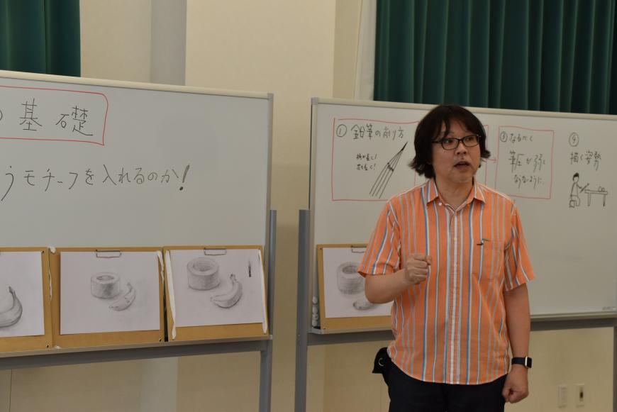 ホワイトボートの前に立つ齋氏が話をしている様子の写真