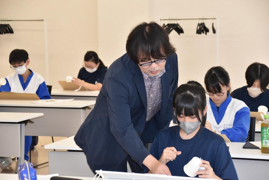 女子生徒が描いたデッサンを齋氏が指導しており、女子生徒が真剣な表情で見ている様子を写した写真