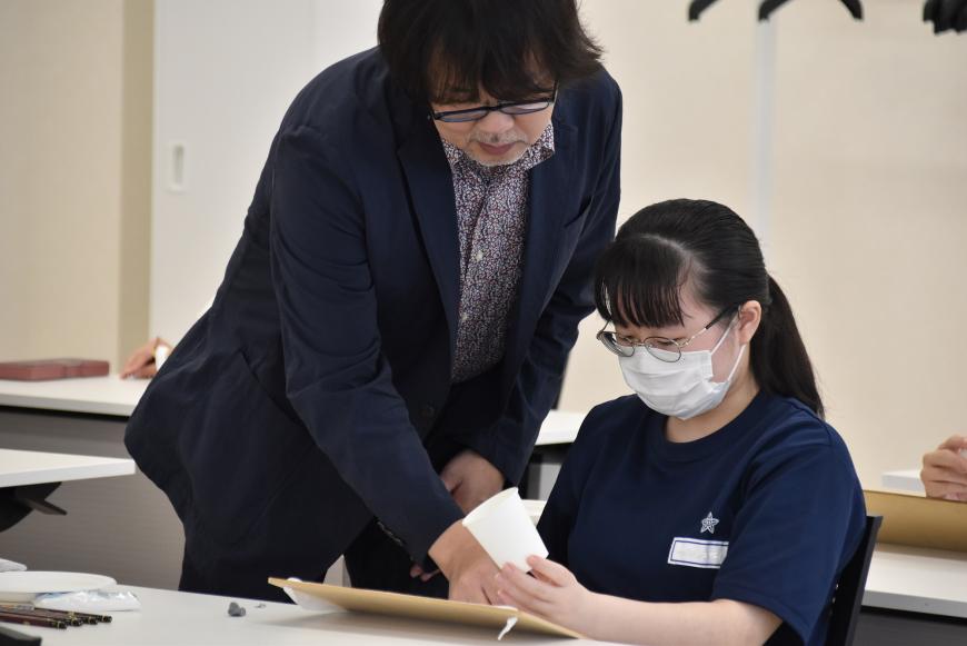 女子生徒のデッサンしている絵を指さし齋氏が指導している様子を写した写真