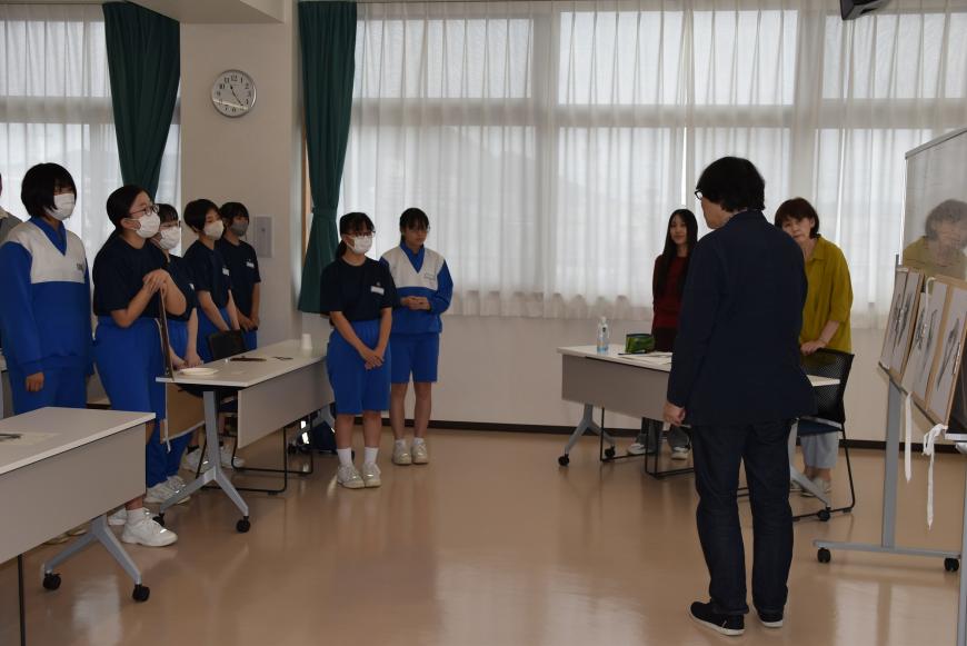 前方のホワイトボードに生徒の作品が並んでおり、生徒を前に齋氏が話をしている様子の写真
