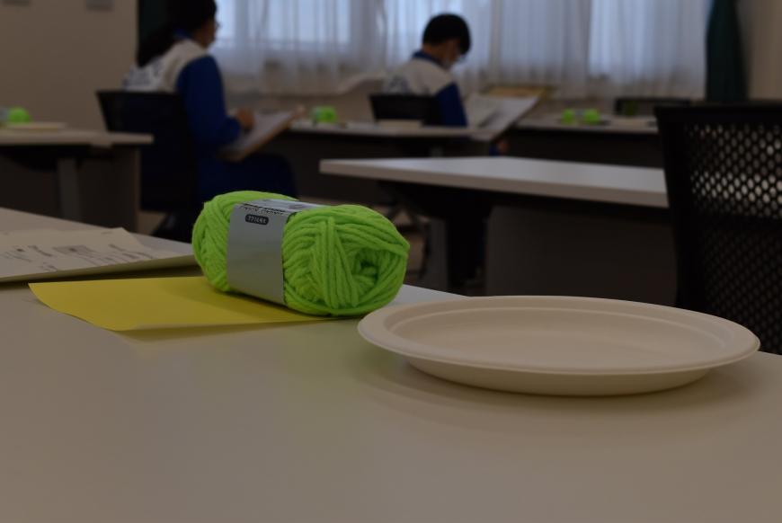 黄色い折り紙の上に黄緑色の毛糸玉が置かれている写真