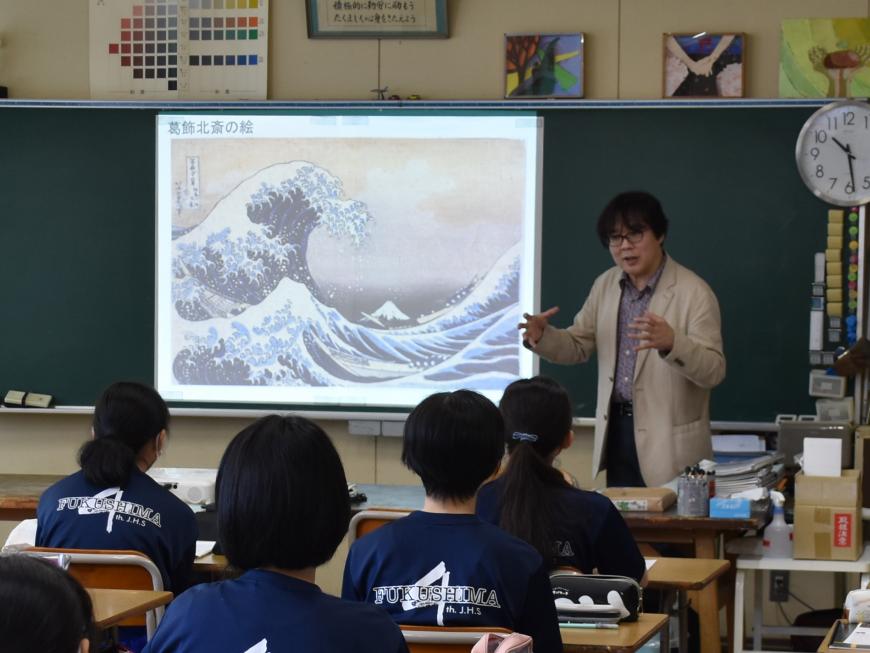 葛飾北斎の波の絵が黒板のスクリーンに映され、齋氏が熱心に生徒の皆さんへ話をしている様子を写した写真