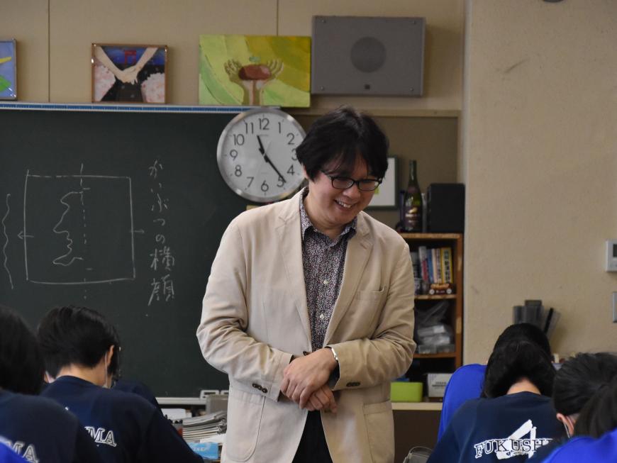 生徒が座っている席の周りを笑顔で歩いている齋氏の写真