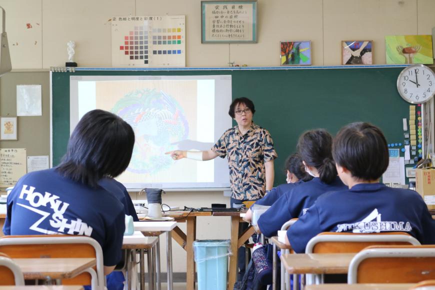 黒板のスクリーンに映しだされた映像を指さしながら、齋氏が生徒の皆さんに話をしている様子の写真