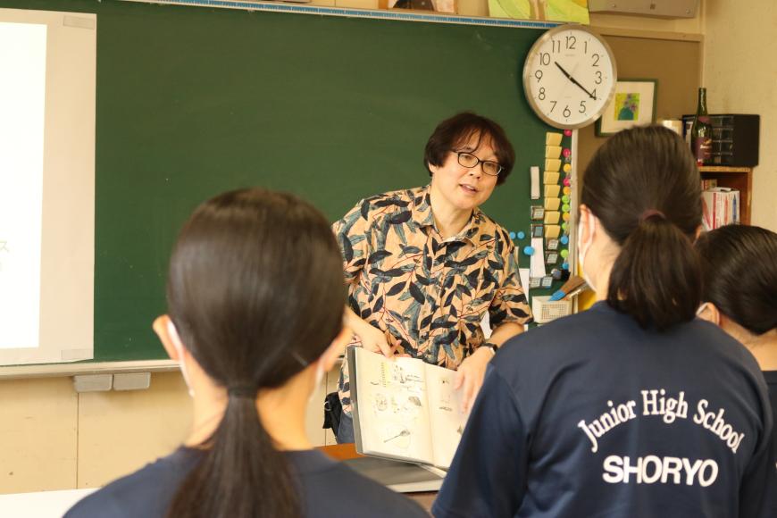 齋氏が資料の本を広げながら、生徒の皆さんに話をしている様子の写真