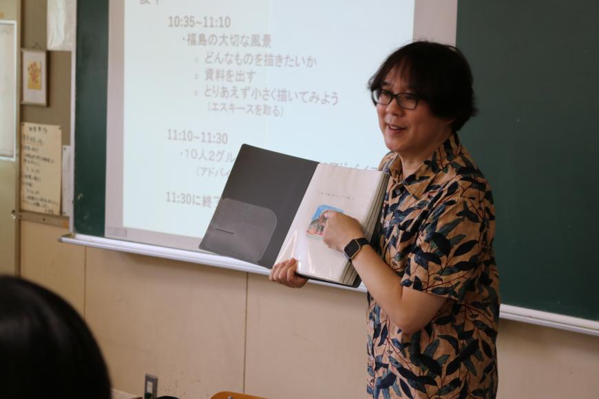 齋氏が手に持っている資料を指さしながら生徒の皆さんに話をしている様子の写真