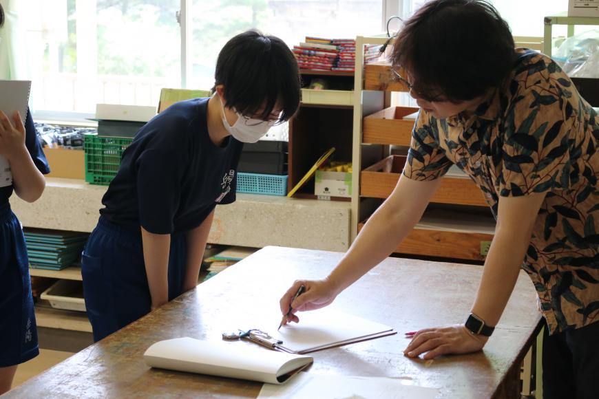 齋氏が紙に書き込みながら、生徒の一人を直接指導をしている様子を写した写真