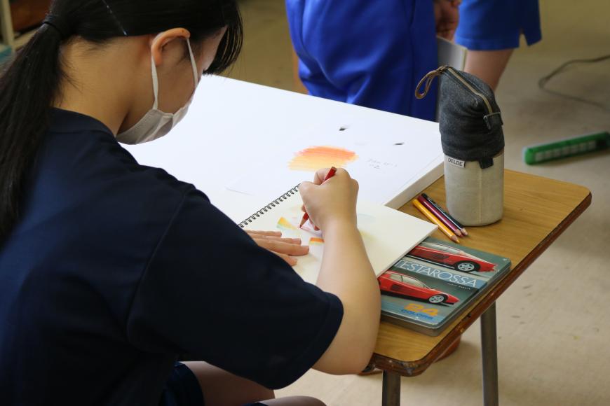 自席に座っている女子生徒がスケッチフックに描いている絵に色を塗っている様子を写した写真