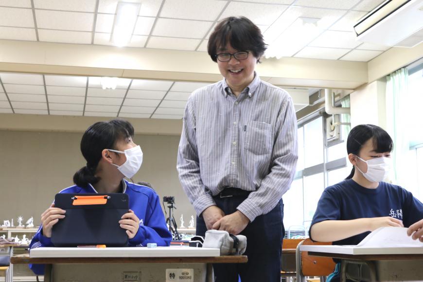 女子生徒の横に立ち、笑顔で対応している齋氏の写真