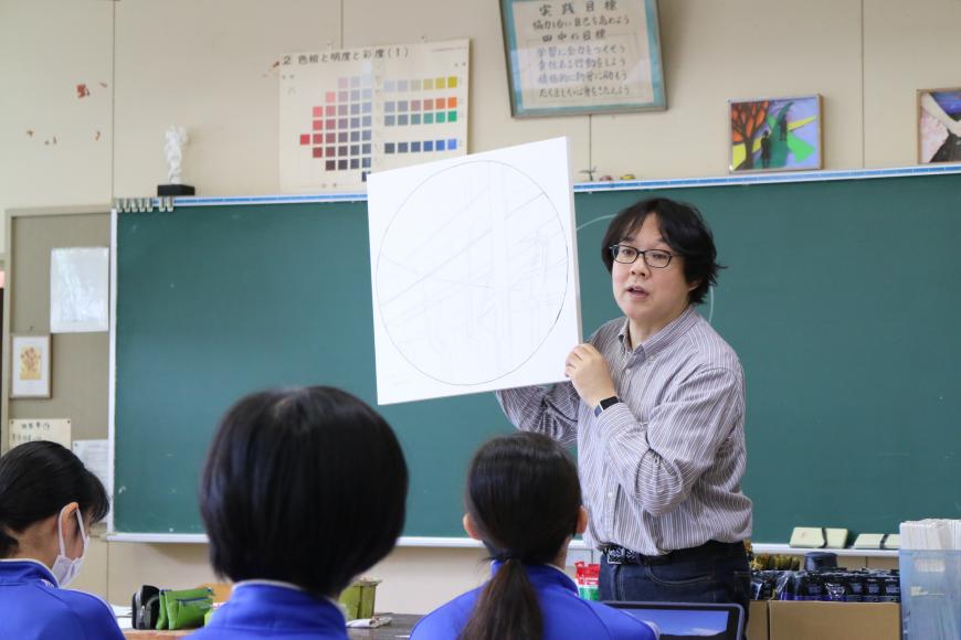 大きな丸が描かれた画用紙を齋氏が持って、生徒に見せながら話をしている様子の写真