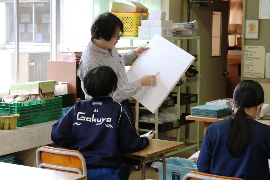 齋氏が画用紙に鉛筆で描きながら、一人の生徒に直接指導している様子を写した写真
