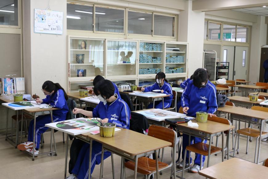 自席に座り、絵具を使って作品の色付けを集中して行っている生徒の皆さんを写した写真