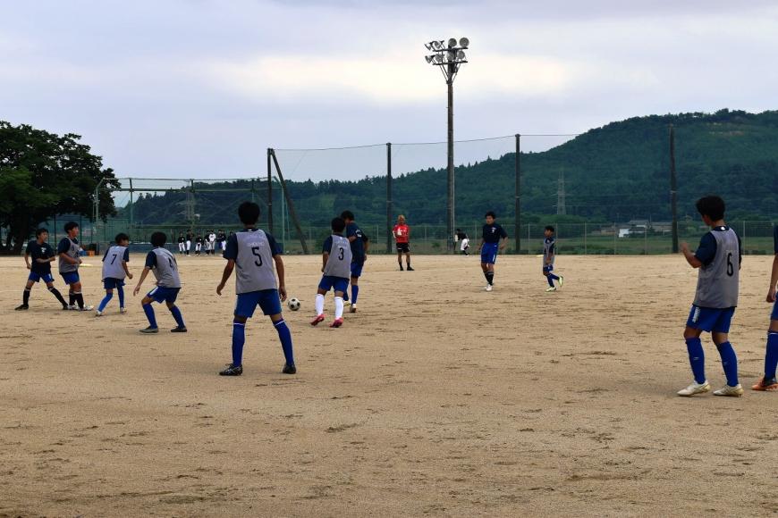 2チームに分かれた部員たちがグラウンドに広がって、ボールの動きを見ながらサッカーをしている様子の写真