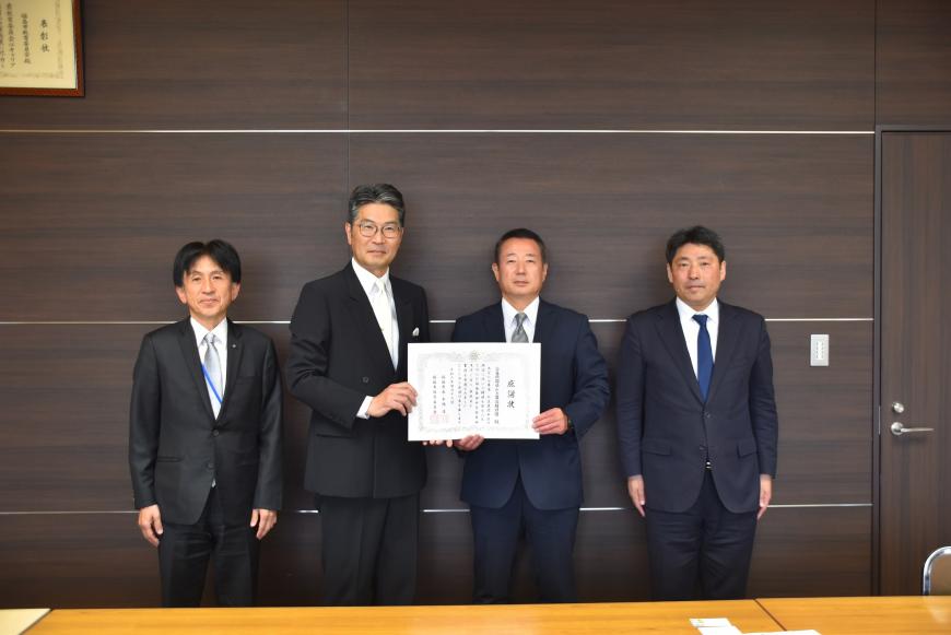 中央の市長と男性が感謝状を持ち、関係者2人と横一列に並んでいる記念写真