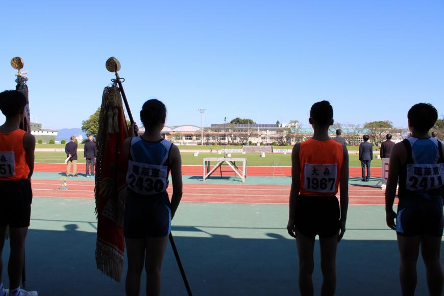 青空の下、2名が優勝旗を持っており、選手4名がグランド側を見ている後ろ姿の写真