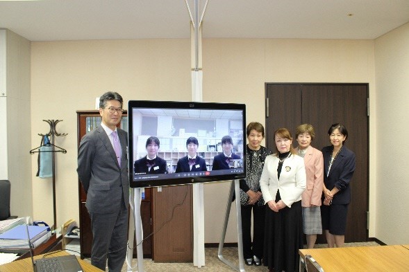 3名の学生が映し出されたモニターを挟んで左側に市長、右側に女性4名が立っている記念写真