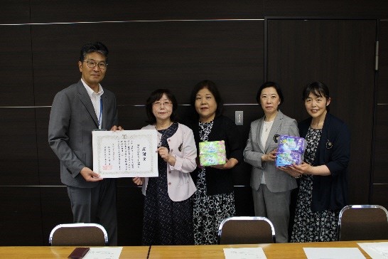 市長と女性が賞状を持ち、女性3名が寄贈していただいた生理用品を持って記念撮影している写真