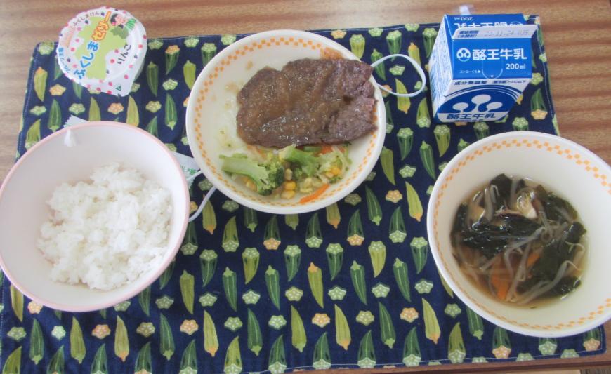 オクラ柄のランチマットに、ごはん、県産牛ステーキのおろしソースかけ、ブロッコリーサラダ、五目スープ、県産りんごゼリーが並べて置かれている写真