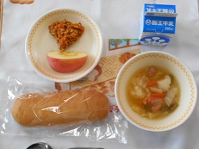 パン、スープ、リンゴ、揚げ物、牛乳がランチマットの上に並んだ写真