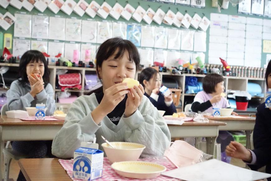 配膳されたリンゴを両手で持ちじっと見ている女の子の写真