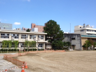 土のグラウンドの左側に2階建ての白い校舎がたっている福島第一小学校の外観写真