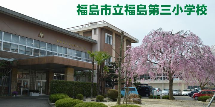 茶色の壁の2階建ての校舎前に低木の植栽や大きな枝垂桜の木がある福島第三小学校の外観写真