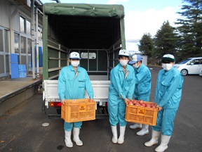 軽トラックの荷台の前で、たくさんのリンゴが入ったかごを持つ、水色の作業着を着た福島明成高等学校の生徒の皆さんの写真