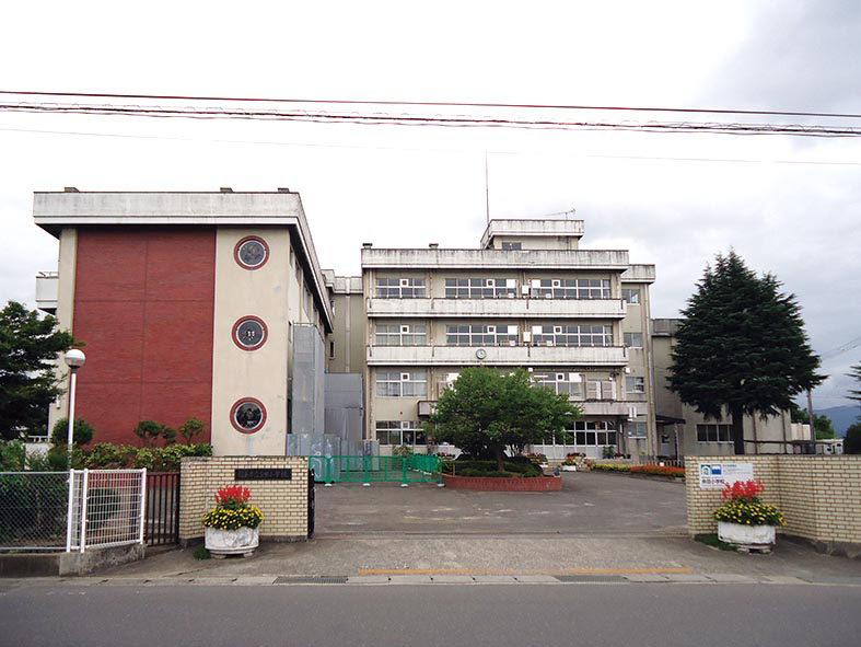 門の中のコンクリートの敷地に3階建て、4階建ての校舎や植栽がある余目小学校の外観写真