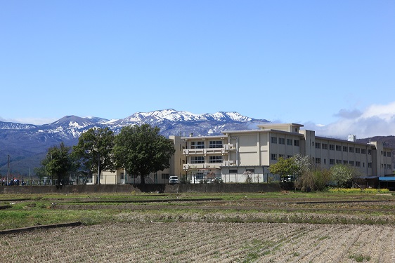 田畑が広がる中、雪の積もった山脈を背に、3階建ての校舎が敷地内に複数建つ笹谷小学校の写真