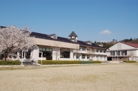 校庭に面して2階建ての校舎があり奥に体育館がある平石小学校の外観写真