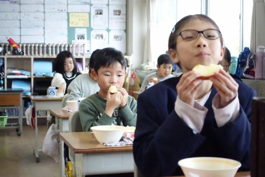 両手に持ったリンゴを嬉しそうに食べている女子生徒の写真