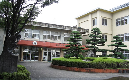 2階建ての校舎横に3階建ての校舎が併設され、入り口前に植栽がある岳陽中学校の外観写真